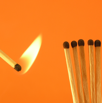 The Spark That Can Set Off a Crisis A single lit match approaching a row of unlit matches, symbolizing the chain reaction risk of overdependence on government funding.