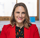 Professional headshot of Glennda Testone, smiling and wearing a red blazer, set against a soft, neutral background.