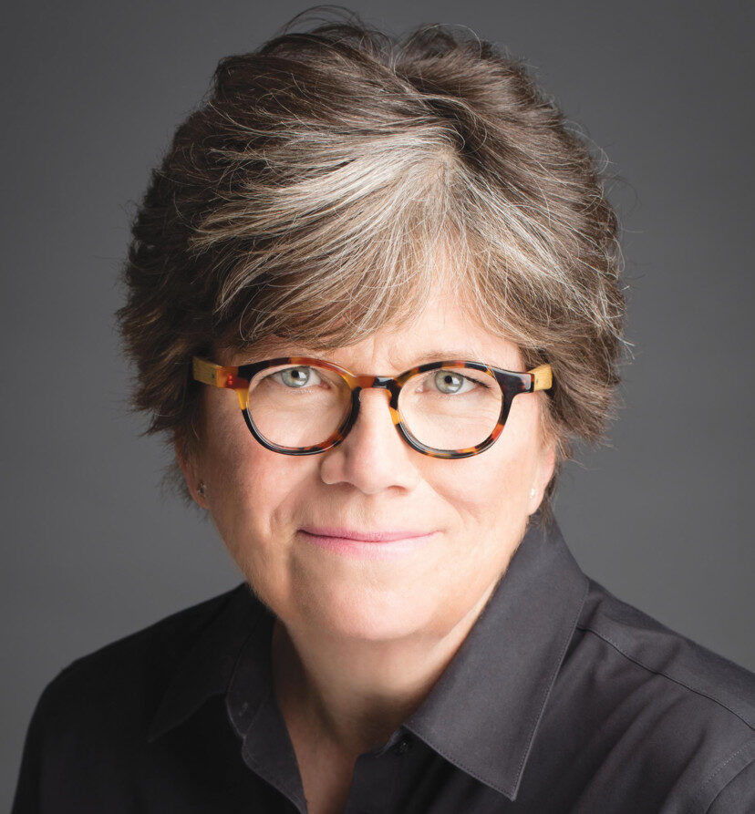 Headshot of Joan Garry nonprofit leadership coach and founder of the Nonprofit Leadership Lab, a woman with short, graying hair and glasses, wearing a dark shirt, smiling gently against a plain gray background.