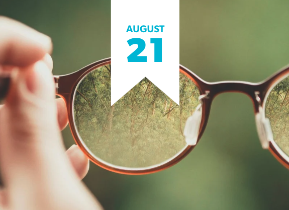 Expanding Perspectives on Earned Revenue A hand holds a pair of round, light brown-framed glasses with yellow-tinted lenses. Through the lenses, a blurry green background of trees or foliage is visible. A white banner hangs vertically from the top, partially obscuring the view, with the words "AUGUST 21" in blue text.