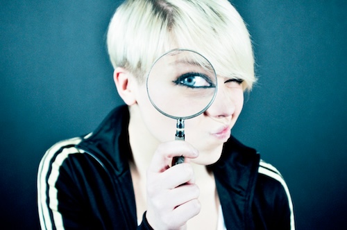Identify Board Challenges A woman looks through a magnifier at the viewer to examine more closely.