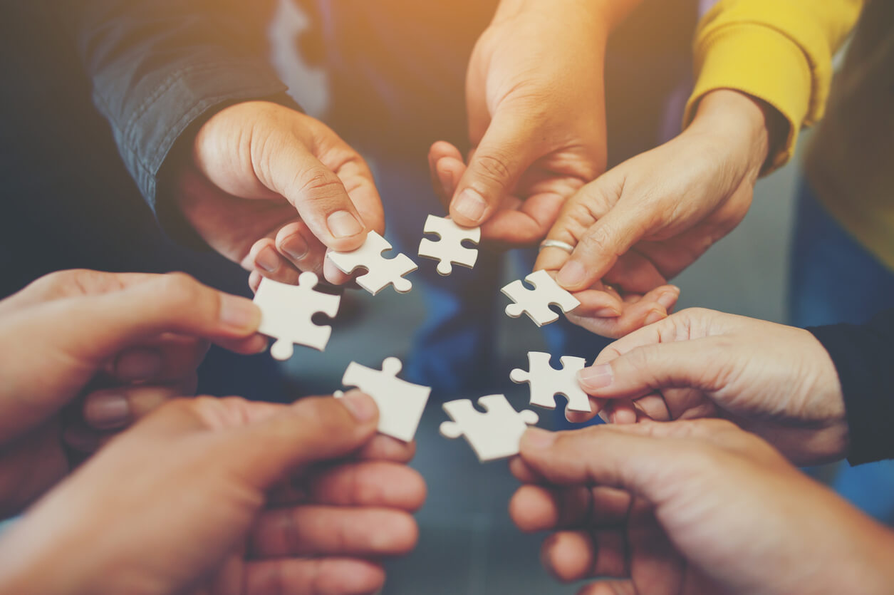 A group of hands comes together in a circle, each holding a single puzzle piece.